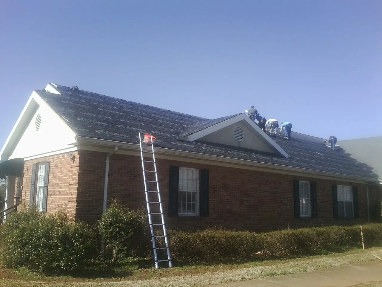 Crew tearing shingles off a brick ranch roof with a ladder set — Metal Roof Repair work by our crew in Emeryville
