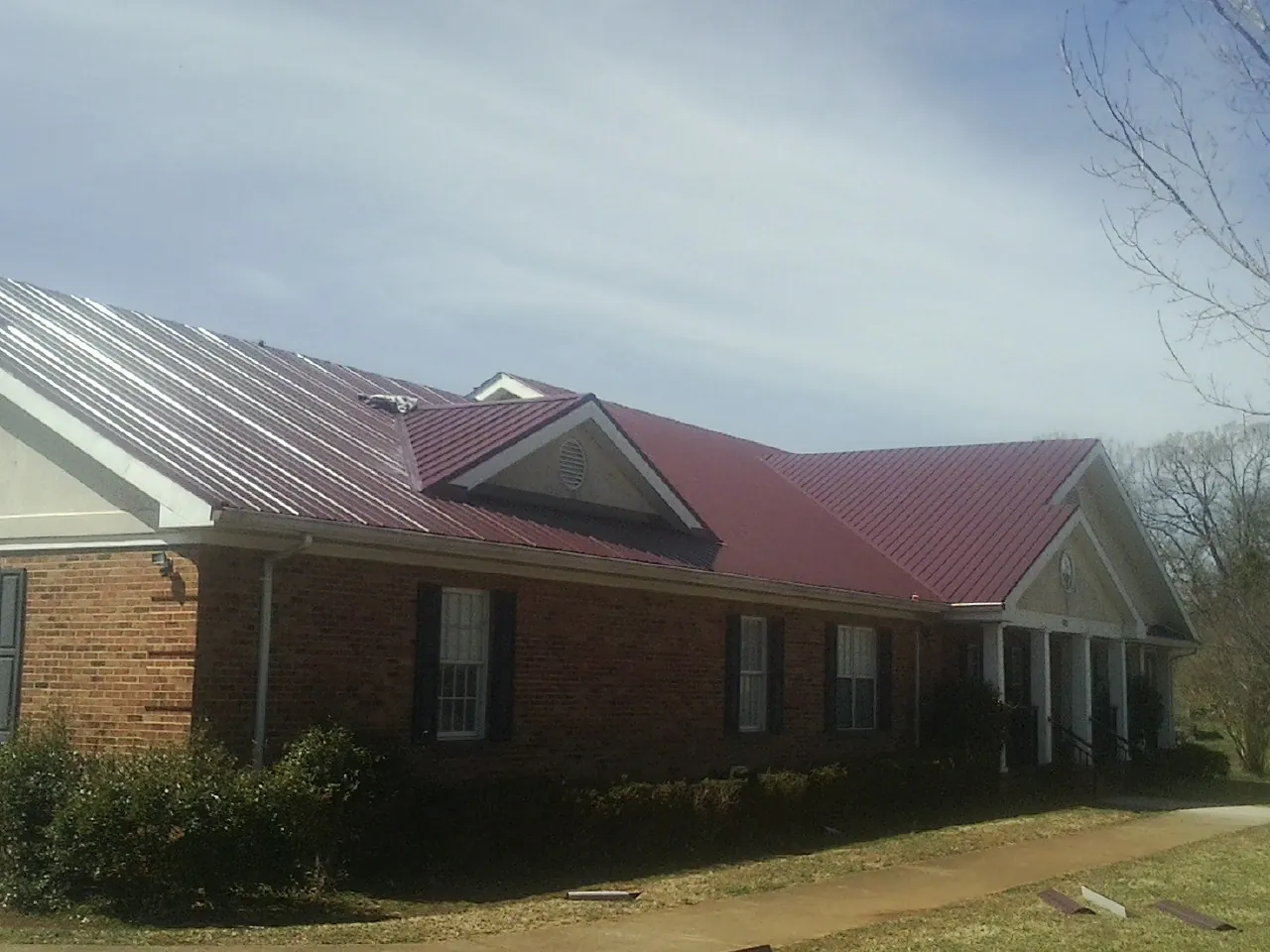 Red metal roof with gabled entries on a long brick building, from a Hail Damage Roof Repair job in Emeryville
