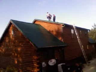 Crew on the ridge of a green metal roof on a two story log home in Emeryville