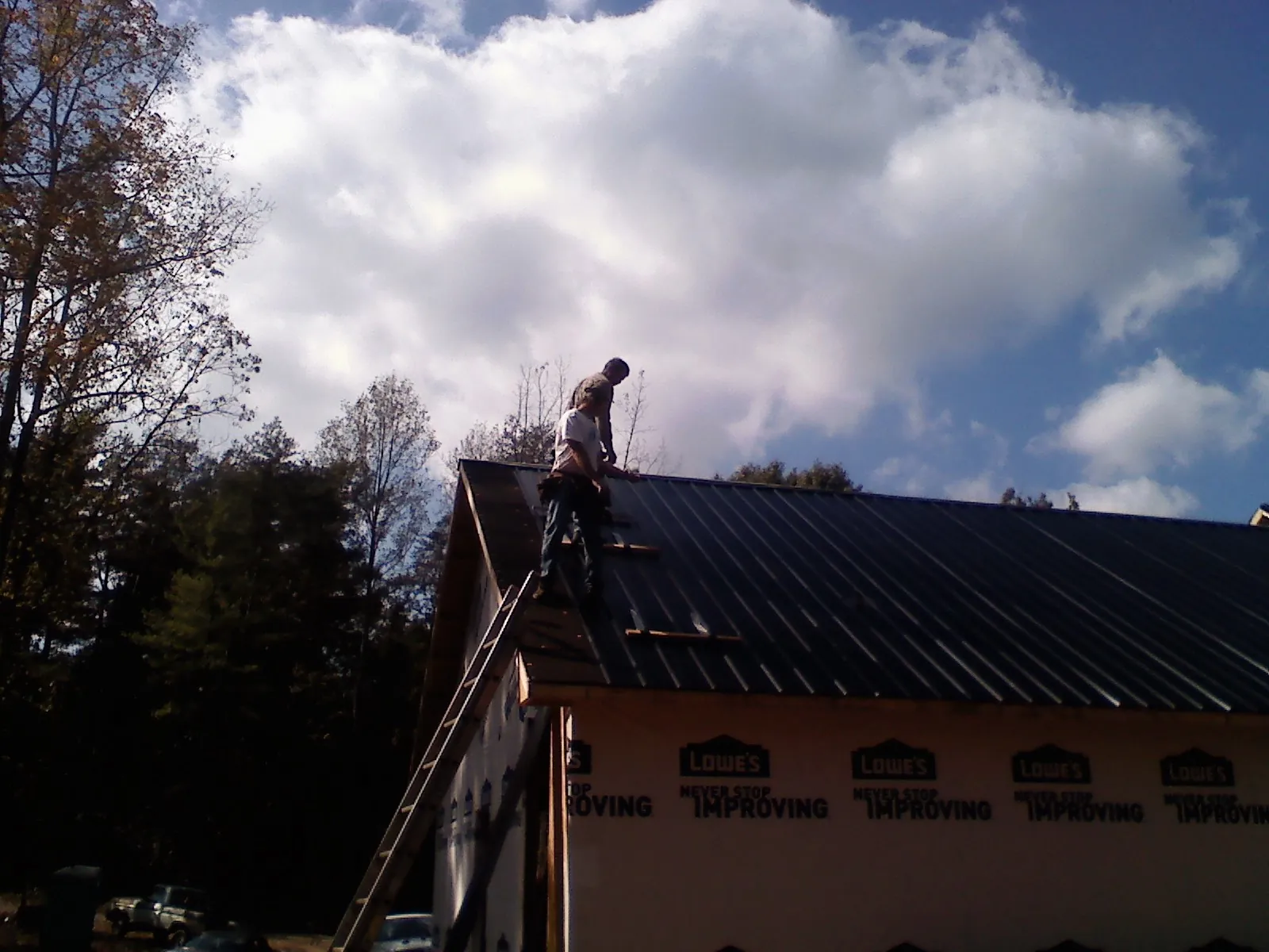 Roofer fastening dark metal panels high against a cloudy sky, from a Roof Inspection job in Emeryville