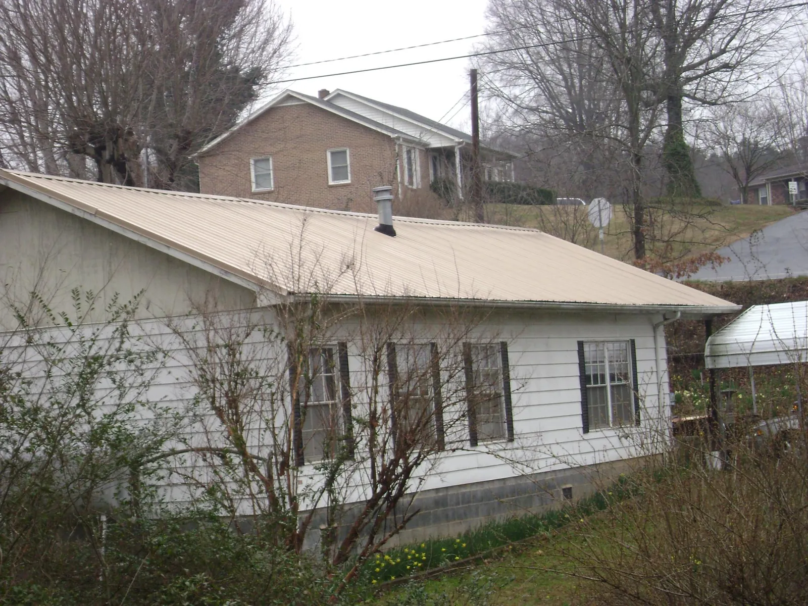Tan metal roof on a white sided house set into a hillside — Commercial Roofing by Roofing Brothers in Emeryville