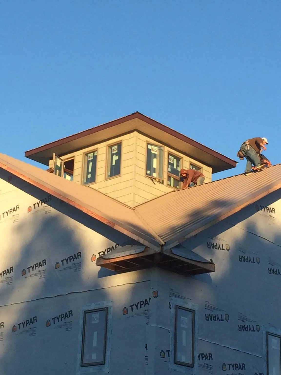 Roofers working around a rooftop cupola on a new metal roof at sunset — Roof Waterproofing in Emeryville by Roofing Brothers